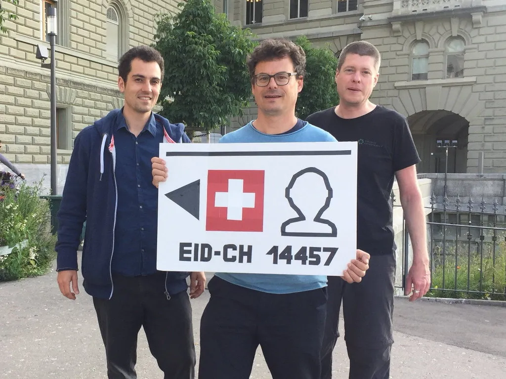 Drei Männer vor dem Bundeshaus mit einer selbst gebastelten E-ID «EID-CH 14457»